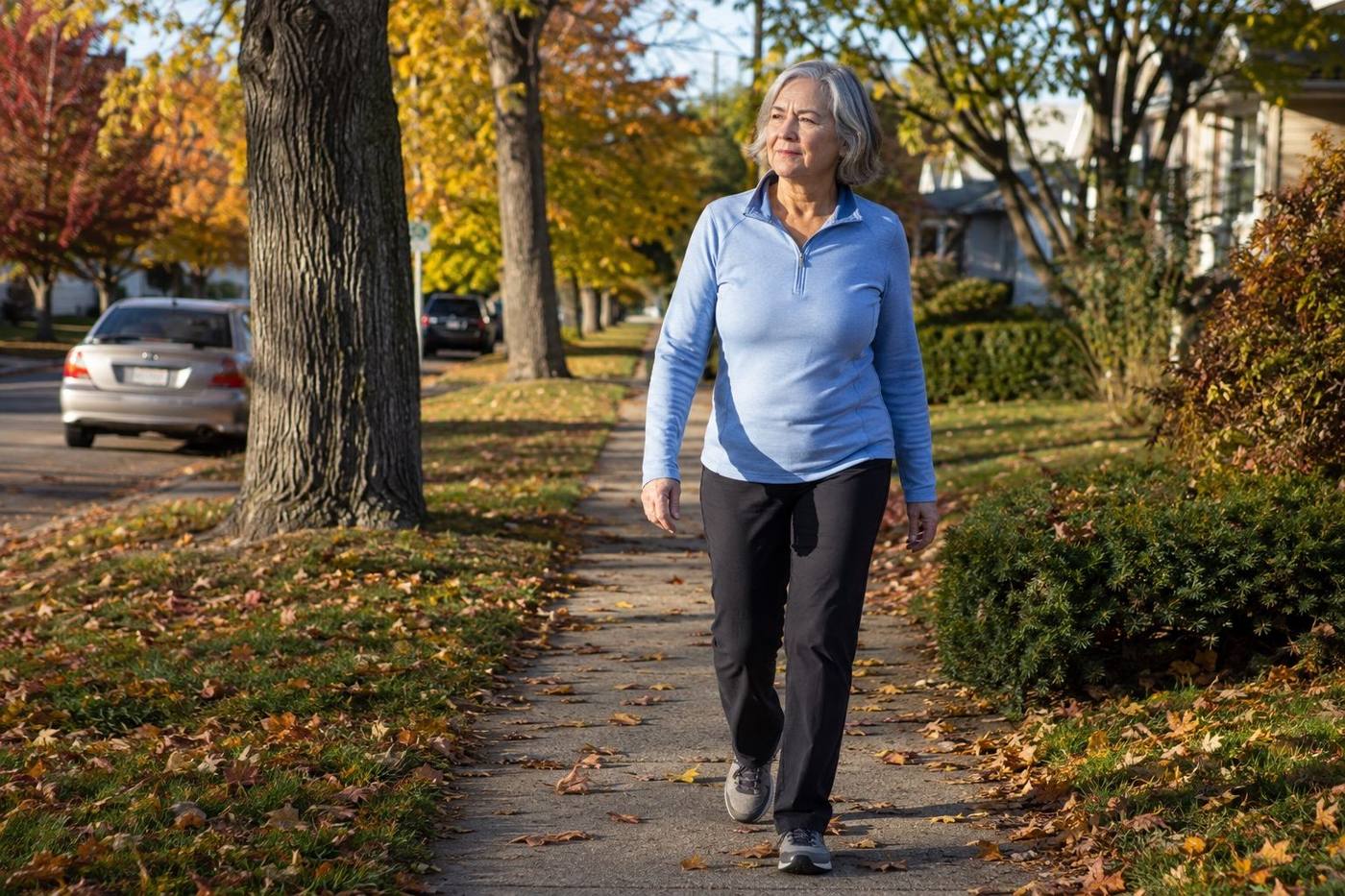 A woman in her sixties walking on a tree-lined sidewalk on an autumn morning